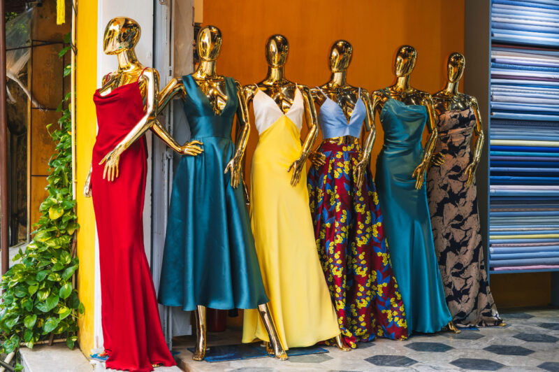 A group of mannequins in bright elegant dresses stands outside a women's clothing store
